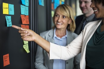 Two Women and Man Standing in Front of Wall Board