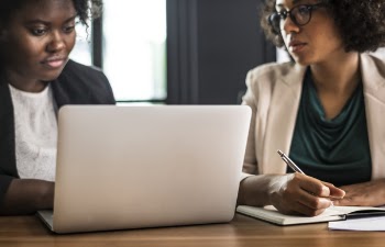 Two Women Sitting on Chair in Front of Laptop on Table Inside Room