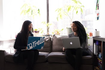 Two Women Sitting on Gray Fabric 2-seat Sofa Staring at Each Other While Carrying Laptop Computers