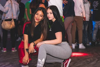 Two Women Smiling and Almost Sitting Surrounded With People