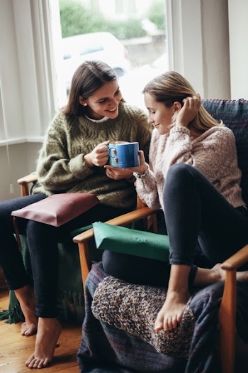 Two Women Smiling and Talking While Sitting on Chair and Holding a Mug