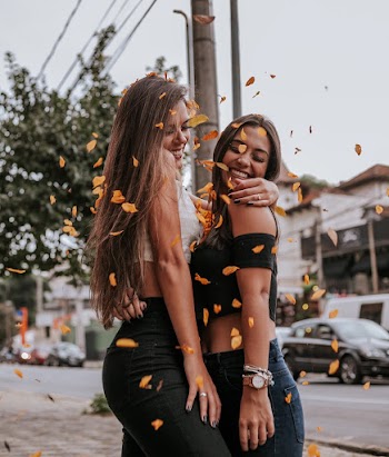 Two Women Standing Beside Street Under Falling Dried Leaves
