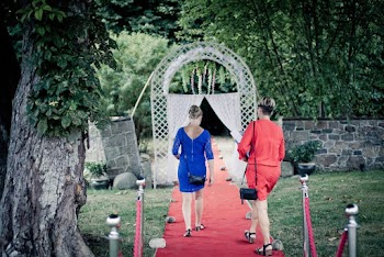 Two Women Walking on Red Carpet Leading Inside White Gate