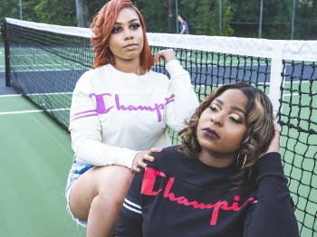 Two Women Wearing Champion Sweaters Leaning on Tennis Net