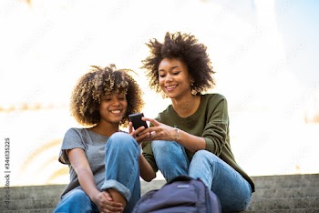two young african american women sitting on steps outside looking at cellphone