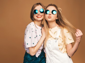 Two young beautiful smiling blond hipster girls in trendy summer colorful t-shirt clothes. sexy carefree women posing on beige background in round sunglasses. positive models having fun Free Photo