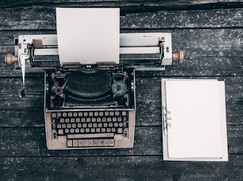 type writer beside clipboard on wooden surface