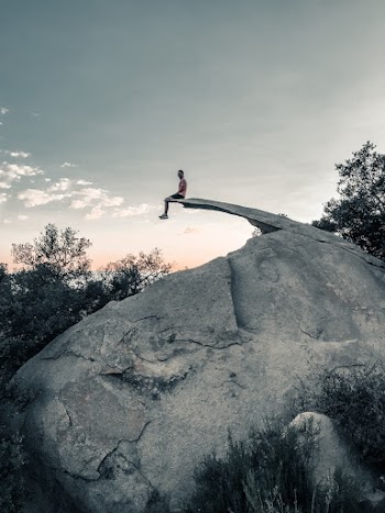 Unknown Person Sitting on Gray Rock Formation