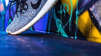 unpaired gray and white Nike sneaker leaning on concrete wall with graffiti