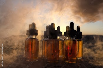Vape concept. Smoke clouds and vape liquid bottles at sunset time. Blured background. Light effects. Useful as background or vape advertisement or vape