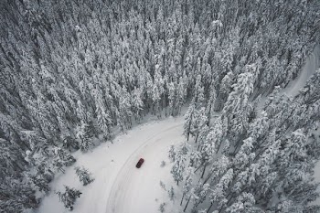 vehicle speeding on road covered in snow surrounded by trees at daytime