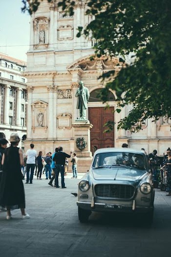 vehicle surrounded by people near standing man statue during daytime