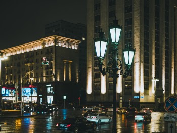 Vehicles Speeding in Road Near Building With Lights at Nighttime