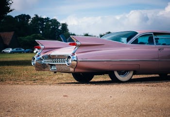 vintage pink muscle car parked near field of grass