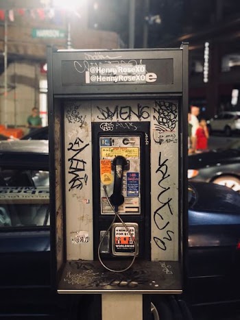 vintage rectangular black and grey telephone booth overlooking people in front of beige building