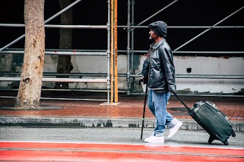 Walking Man in Black Leather Jacket and Blue Denim Pants Holding Luggage Bag