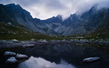 Water Besides Grey Stone Near Green Grass and Mountain during Cloudy Day