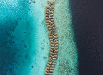 Water bungalows spreading across the beautiful Maldivian reef with a turquoise lagoon on the left and the deep blue on the right. 