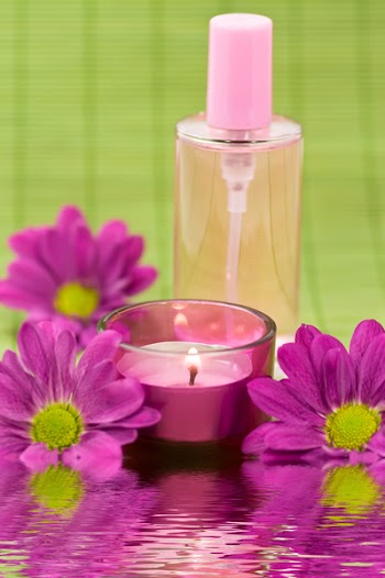 Wellness scene with fragrance bottle, candle and flowers on green bamboo with water reflection