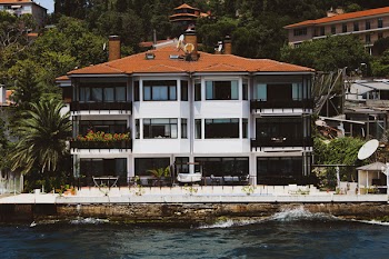 White and Black Concrete House Surrounded by Green Trees Beside Body of Water