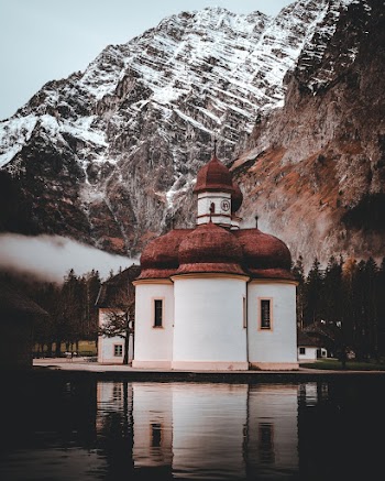 White and Brown Concrete Building Beside Body of Water and Snow-capped Mountain