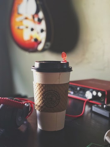 White and Brown Labeled Plastic Coffee Cup on Brown Tabletop Near Black Multimedia Player