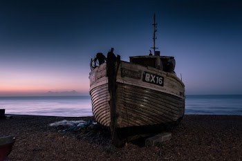 white and gray ship on sand near body of water under orange and gray sky