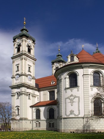 White and Orange Painted Building With Tower Near Leafless Tree Under White Clouds and Blue Sky