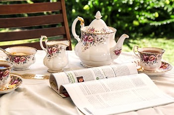 White and Pink Floral Ceramic Tea Set on White Textile Covered Table Beside White and Black Printed Book