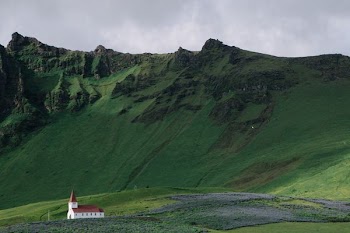 white and red concrete building near green grass field mountain during daytime