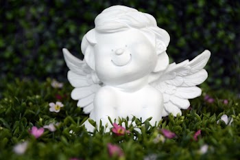White Angel Ceramic Figurine on Green Grass With White and Purple Flower