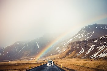 white car travelling near mountains with rainbow