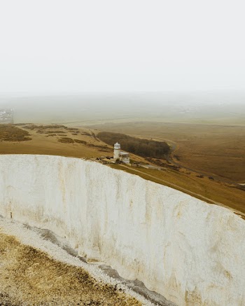 White Concrete Lighthouse On The Edge Of A Mountain Cliff