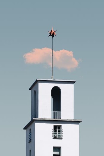 white concrete tower with star-like topper under cloudy blue sky