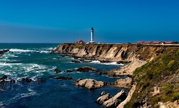 White Lighthouse Near Body of Water Under Blue Sky during Daytime