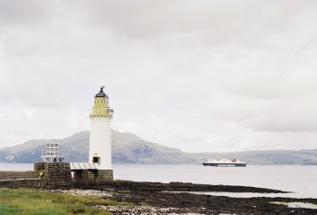 White Lighthouse Near Body of Water Viewing Mountain Under White Sky