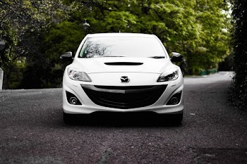 white Mazda vehicle on road near tree