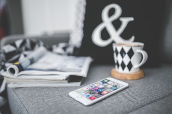 White mobile phone lying on a couch with cup and stack of magazines