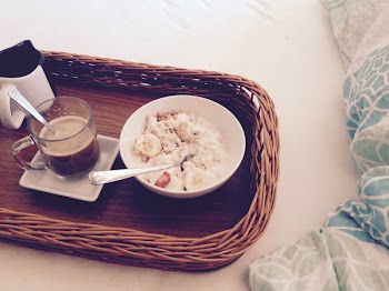 White Round Bowl With Rice and Sliced Bananas Near Clear Glass Mug on Square Ceramic Plate and White and Black Ceramic Mug on Brown Wicker Rectangular Tray