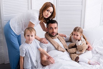 Wife and children taking care of sick father in bedroom, looking at camera