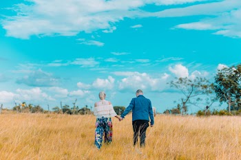 Woman and Man Holding Hands Walking on Brown Grass Field