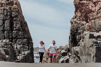 Woman and Man Holding Hands While Walking Between Rock Formation