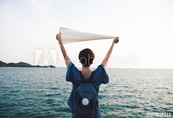 Woman arms raised and holding flag by the sea in rear view