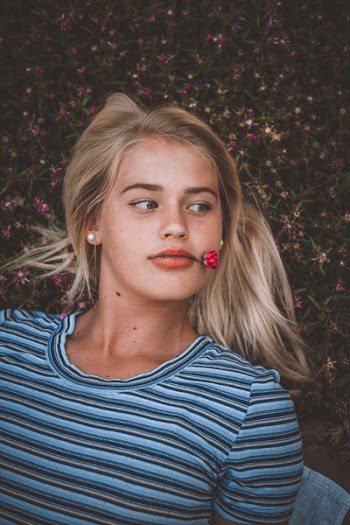 Woman Biting Red Flower While Lying on Ground