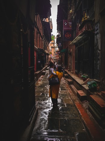 Woman Carrying Girl Between Concrete Building Durng Daytime