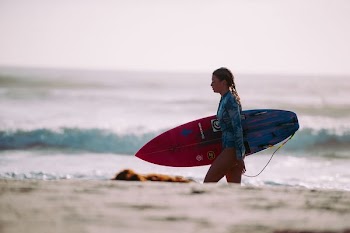 woman carrying red and blue surfboard walking on shore during daytime