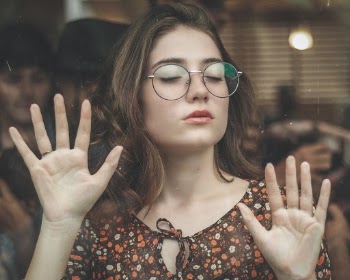 Woman Closing Her Eyes While Leaning On Clear Glass Wall