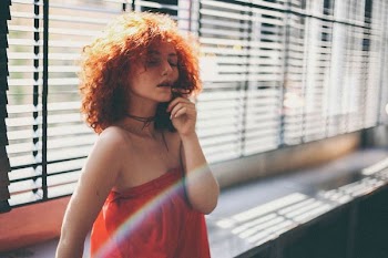 woman closing her eyes while leaning on window inside room during daytime