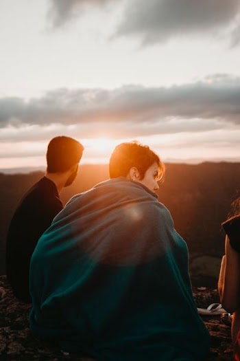 woman covering green textile near man sitting during sunrise