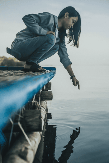 Woman Crouching on Dock Pointing at Water